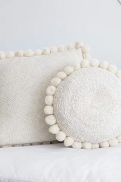 two white pillows with pom - poms on them sitting on a bed next to a lamp