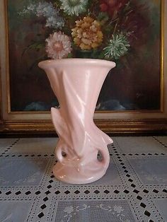 a pink vase sitting on top of a table next to a painting