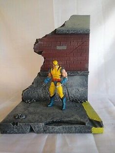 a toy figurine is posed on top of a piece of concrete with a brick wall in the background