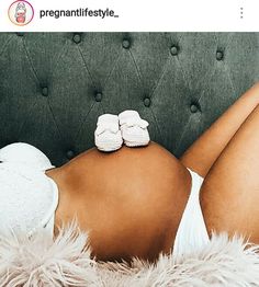 a pregnant woman laying on top of a couch wearing white slippers and holding her baby booties