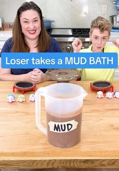 a woman and boy sitting at a table with a mug in front of them that says, loser takes a mud bath