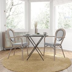 a table with two chairs and a vase on it in front of a window near a rug