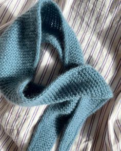 a blue knitted scarf laying on top of a striped bed sheet with the end rolled up