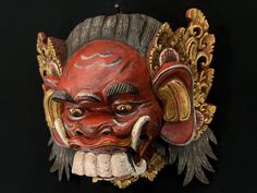 a red mask with gold accents on it's face and two horns sticking out from its mouth