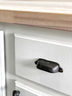 a close up of a cabinet door handle on a white kitchen island with black knobs