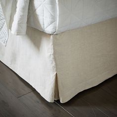 a bed with a white cover and pillows on top of it, next to a wooden floor