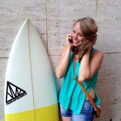 a woman standing next to a white and yellow surfboard talking on her cell phone