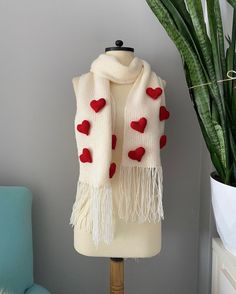 a white scarf with red hearts is on a mannequin next to a potted plant