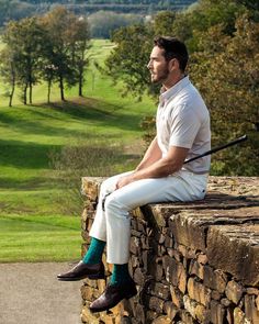 a man sitting on top of a stone wall next to a lush green field and golf course