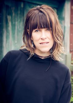 a woman with bangs standing in front of a wooden door wearing a black shirt and earrings