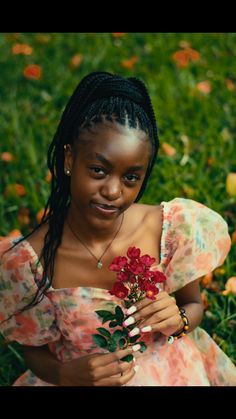 a woman sitting in the grass with flowers on her hand and looking at the camera