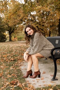 a woman is sitting on a bench in the park with her legs crossed and wearing brown boots