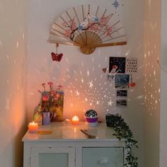 a white cabinet with candles and pictures on the wall behind it, in front of a fan