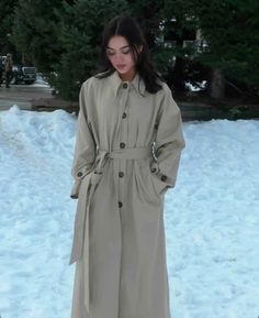 a woman standing in the snow wearing a trench coat