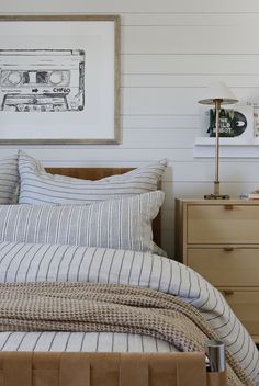 a bed with striped sheets and pillows next to a painting on the wall above it