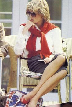 a woman sitting in a chair with her hand on her chin, wearing sunglasses and a red scarf