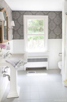 a bathroom with white tile floors and gray wallpaper, along with a large window