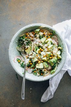 a salad with avocado, corn and other vegetables in a bowl on a table