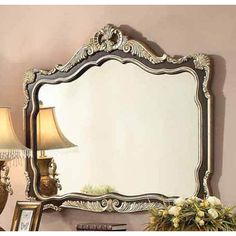 a mirror sitting on top of a dresser next to a lamp and vase with flowers