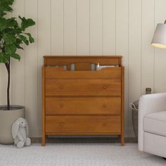 a baby crib next to a white chair and potted plant