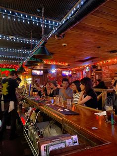 many people are sitting at the bar with their drinks in front of them and lights hanging from the ceiling