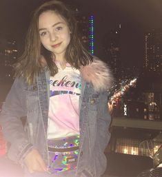 a girl standing in front of a city skyline at night with her hands on her hips