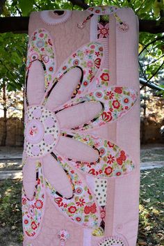 a pink quilt hanging from the side of a tree with lots of flowers on it