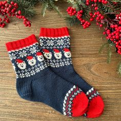 two knitted christmas stockings sitting on top of a wooden floor next to holly branches