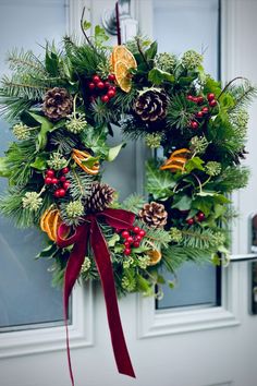 a christmas wreath with pine cones, holly and oranges hanging on a front door