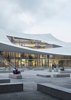 people are sitting on concrete benches in front of a large building that has a white roof