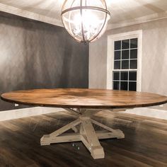 a round wooden table sitting on top of a hard wood floor next to a window