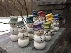 a group of snowmen with hats and scarves on their heads are lined up against a stone wall