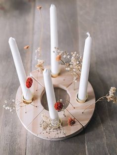 four white candles are arranged on a wooden stand with dried flowers and leaves in the center