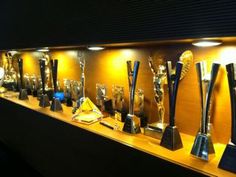 several trophies are lined up on a shelf in a room that is lit by lights