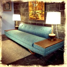 a blue couch sitting next to a lamp on top of a wooden table in front of a painting