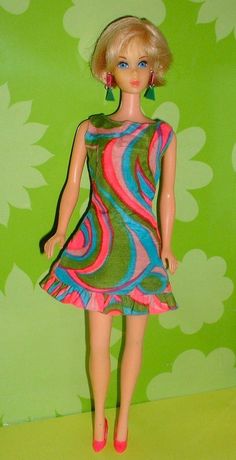 a barbie doll wearing a colorful dress and red shoes standing in front of a green wall