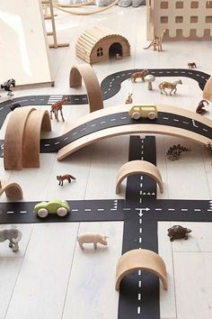 a toy road with cars and animals on it in a playroom area that includes wooden toys