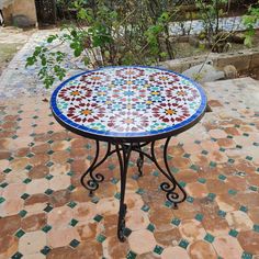 a small table with colorful tiles on it sitting in the middle of a garden area