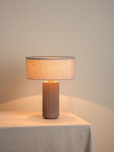 a table lamp sitting on top of a white cloth covered table next to a wall