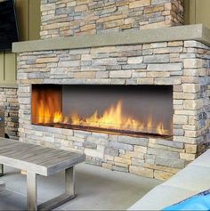 an outdoor fireplace with fire in it next to a picnic table and television on the wall