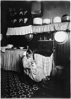 an old black and white photo of a woman sitting in a kitchen