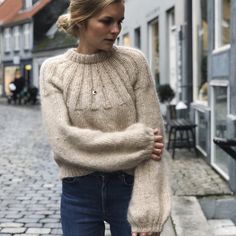 a woman is walking down the street with her hand in her pocket and wearing a sweater