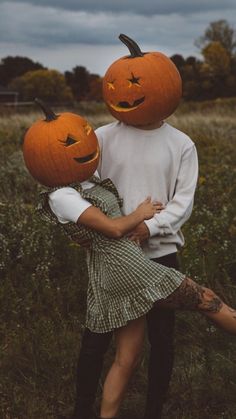 two people wearing pumpkin heads in a field