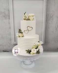 a white wedding cake with flowers and hearts on top is displayed in front of a frame