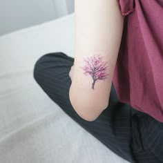 a woman's arm with a small pink tree tattoo on the left inner arm