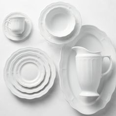 white dishes and cups are arranged on a white table top, with one empty cup in the middle