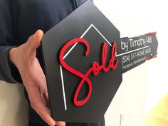 a person holding up a black and red sign with the word sold written on it