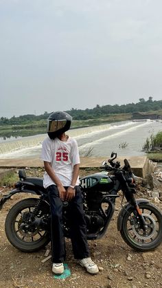 a young man sitting on top of a motorcycle next to a body of water with waves in the background