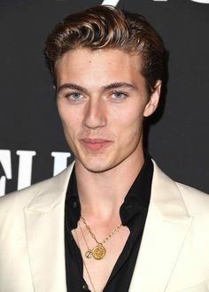 a young man in a white suit and black shirt wearing a gold necklace with a medallion on it