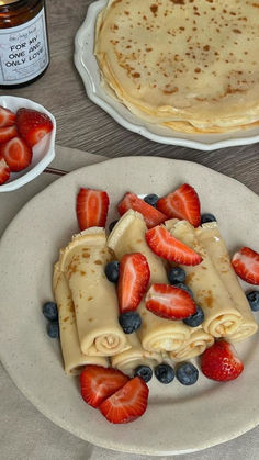 pancakes and strawberries on a white plate with syrup in a jar next to them